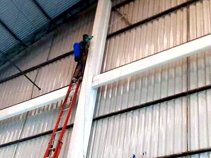 Trabalho em altura sobre escada, dentro de um galpão industrial
