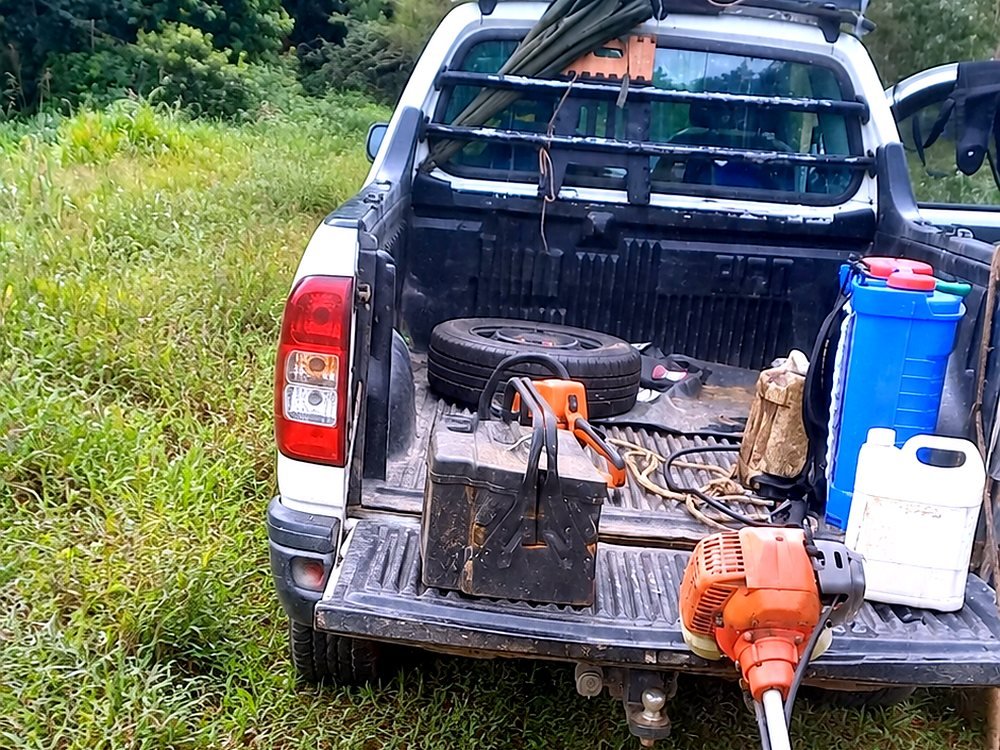 Caçamba da caminhonete do Paulo com roçadeira, pulverizador e galões, em uma propriedade rural